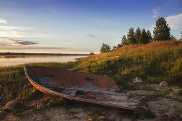 Fototapeta na wymiar old broken boat on the shore of the lake at sunset. Arkhangelsk