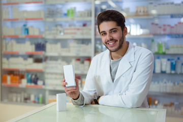 Friendly male pharmacist dispensing medicine holding a box of tablet