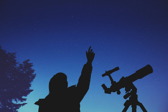 Girl looking at the stars with telescope beside her. 