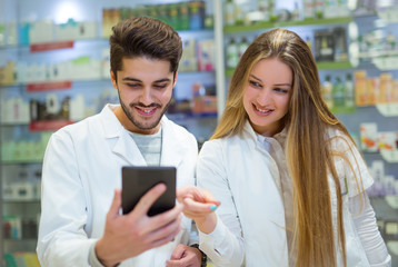 Pharmacists using digital tablet while checking medicine in pharmacy
