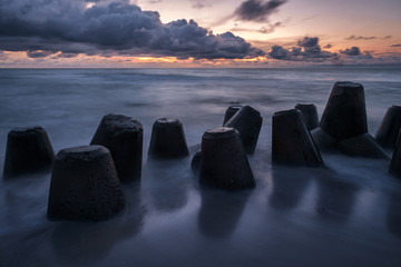 The sun is falling, silhouette of the concrete breakwaters are reflected on the smooth surface of the wet sand at the shore of Curonian spit 