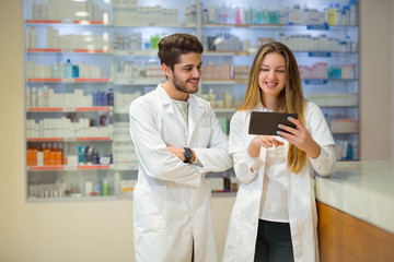 Pharmacists using digital tablet while checking medicine in pharmacy