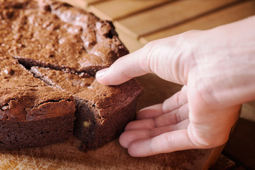 Closeup view of hand taking piece of chocolate brownie cake