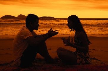 Paar diskutiert am Strand bei Sonnenuntergang - obrazy, fototapety, plakaty