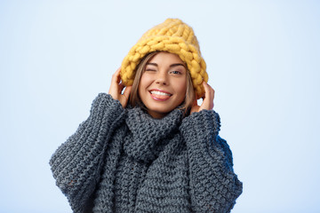 Young beautiful fair-haired girl in knited hat and sweater smiling winking looking at camera over...