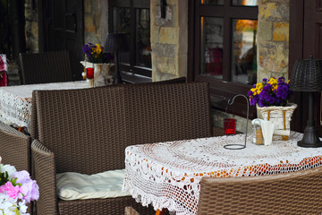 Empty wooden table with a white knitted tablecloth, flowers and chairs at an street cafe