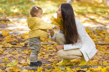 Mother and child playing with leaves in autumn park