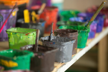 Close-up of silk screen printing ink collection on the shelf hold in plastic containers. Open cans with colorful paints in silkprinting professional workshop print house. Horizontal image