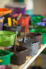 Close-up of silk screen printing ink collection on the shelf hold in plastic containers. Open cans with colorful paints in silkprinting professional workshop print house. Vertical image