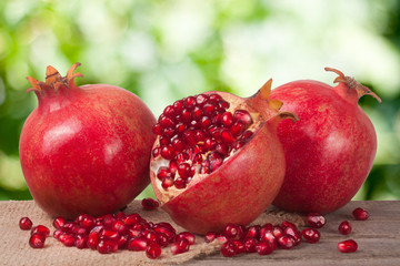 two whole pomegranate and half on the old wooden board with blurred garden background