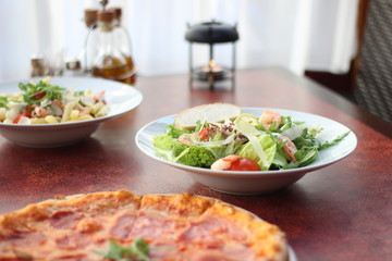 Restaurant food with fresh ingredients - salami pizza and salad with shrimps, parmesan and olive oil