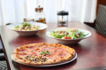 Restaurant food with fresh ingredients - salami pizza and salad with shrimps, parmesan and olive oil