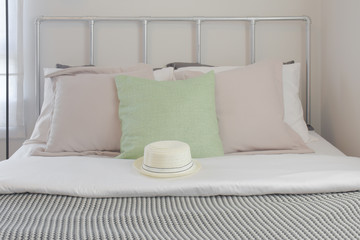 Off-white hat on bed with pastel pillows in background