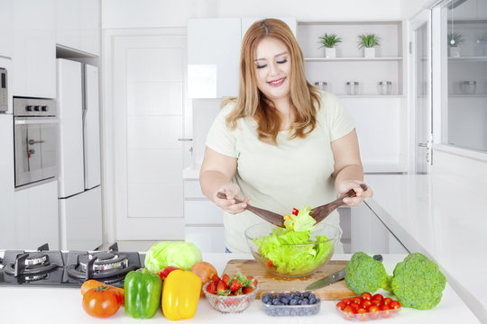 Happy woman making salad at kitchen