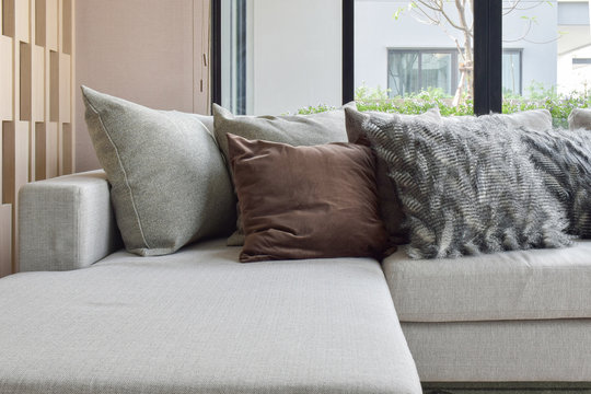 Brown and light gray pillows setting on beige couch  in the corner of living room