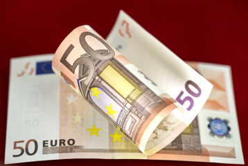 Fifty euros banknotes on red background. One banknote is half ro