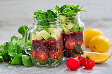 Healthy salad with quinoa, avocado, tomato, red onion, baby spinach, radish and olive oil in a Mason jars.
