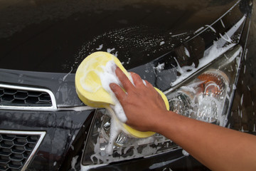 hand of Man washing the car using the yellow sponge with foam