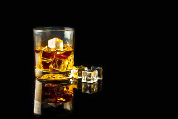 glass of whiskey with ice on a black background with reflection