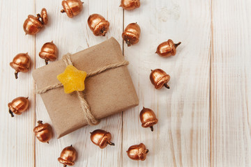 Christmas composition.Present box with twine and craft paper,golden acorns.White wooden table,candy stars.Top view