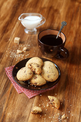 Chocolate Chip Cookies, cup of coffee and pot of milk on wooden table.