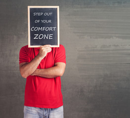 Man holding a blackboard with step out of your comfort zone message written on it
