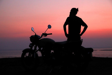 Young man standing near motorbike and enjoying sunset view 
