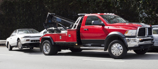 Surprise! Your car is G-O-N-E! Red tow truck hauling away white car. Horizontal.