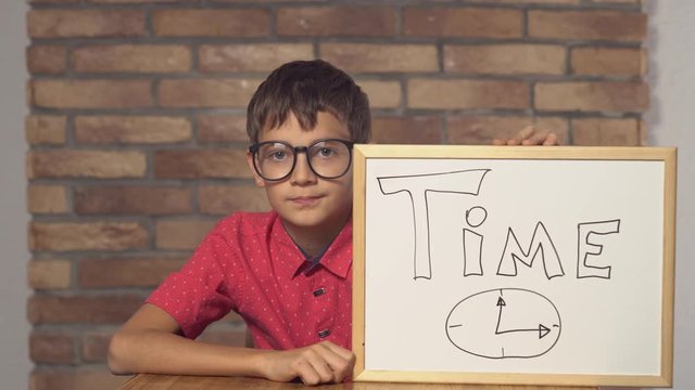 child sitting at the desk holding flipchart with lettering time on the background red brick wall