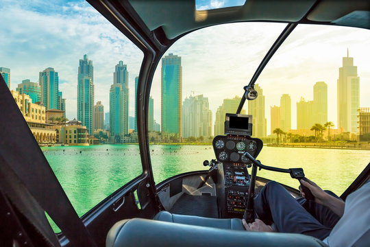 Helicopter cockpit flies in Dubai skyscrapers skyline at sunset, United Arab Emirates, with pilot arm and control board inside the cabin.
