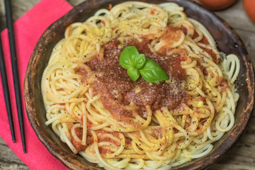 Spaghetti marinara pasta with tomato sauce and basil on rustic hand made ceramic plate on old wooden table.