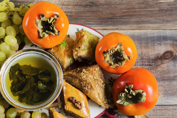 Eastern breakfast. Green tea with sweeties, persimmons, grapes on wooden surface