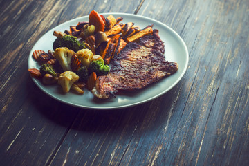 Roasted vegetables and steak served on white plate on dark wooden boards