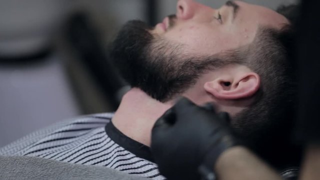 Barber shaves the beard of the client in the barbershop