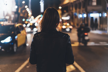 Hipster girl in black leather jacket from back on background illumination glow bokeh light in night...