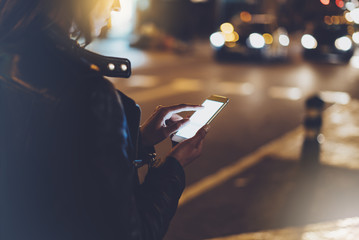 Girl pointing finger on screen smartphone on background illumination glow bokeh light in night atmospheric christmas city, hipster using mobile phone, headlights auto taxi; mockup glitter street