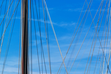 Sailboat mast and ropes in harbor against blue sky