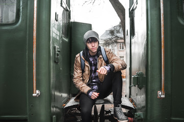 A young guy in a jacket with a backpack near train.