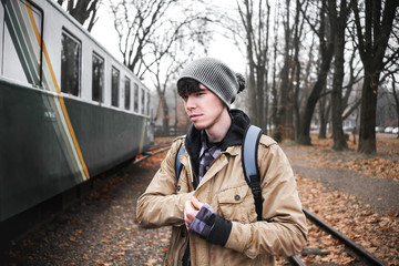 A young guy in a jacket with a backpack near train.
