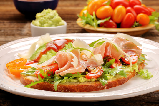 Avocado sandwich on fresh bread with arugula ham tomato and chee