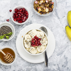 Healthy breakfast oatmeal with pomegranate, bananas, seeds and nuts, overhead scene on white marble. Top view
