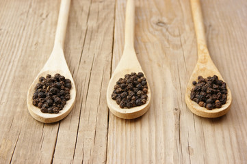 Black pepper in wooden spoon on the old board