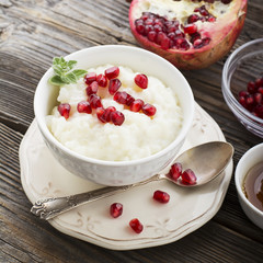 Fragrant warm homemade rice milk porridge with sugar and pomegranate seeds on a wooden background. The concept of healthy, seasonal dishes