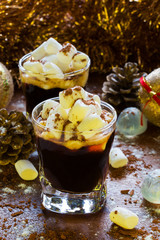 Christmas or New Year decoration and  black coffee in small glasses with marshmallows, cinnamon and icing sugar, fir cones on wooden brown background.
