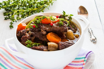 Beef Bourguignon in a white soup bowl. Stew with carrots, onions, mushrooms, bacon, garlic and bouquet garni. The dish is served with fresh thyme.