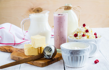 Dairy produce. Milk in bottle, cottage cheese in bowl, kefir in jar, cranberry yogurt in glass, butter and fresh berries. Wooden white table.