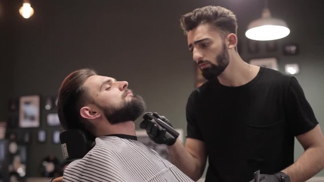 Barber cutting beard with electric razor at a barber shop.