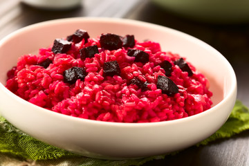 Beetroot risotto prepared with beetroot puree, roasted beetroot pieces on top, photographed with natural light (Selective Focus, Focus on the first beetroot pieces on top of the risotto)
