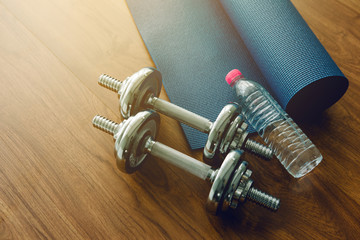 Silhouette Pair of dumbbells with blue yoga mat on wood floor,flare light