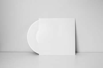 white vinyl record in white paper case put on table and leaning against a wall